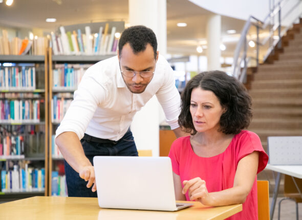 Tutor explaining research specific to student in library